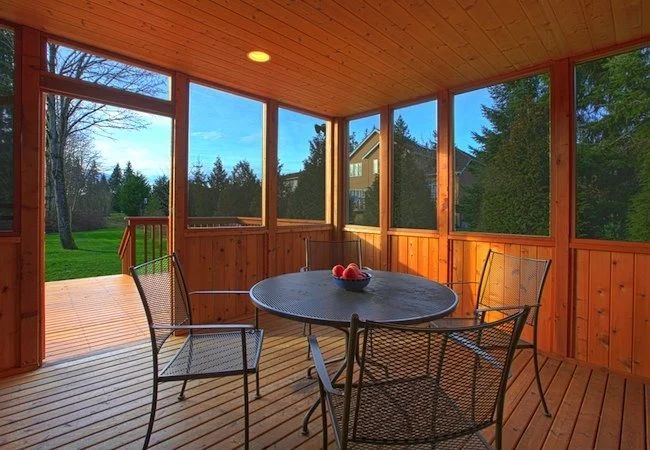 a table and chairs on a porch with wood paneling, glass walls and large windows