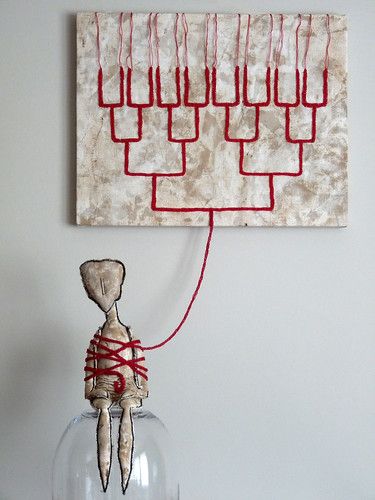 a painting hanging on the wall above a glass vase with a string attached to it