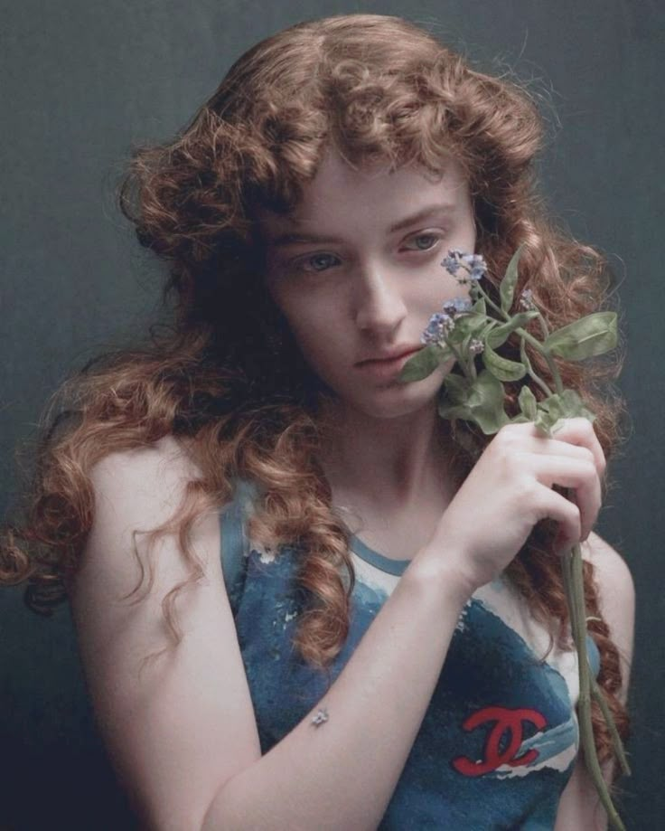 a young woman holding a flower in her right hand and looking down at the camera