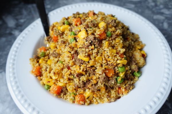 a white plate topped with fried rice and veggies next to a black spoon