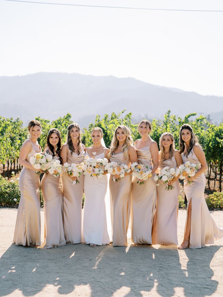 a group of women standing next to each other in front of some vineyard bushes and trees