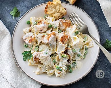 a white plate topped with pasta covered in chicken and peas next to bread on top of a blue table cloth