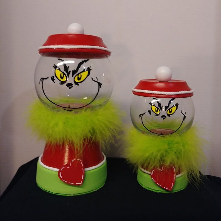 two glass jars with painted faces and green feathers on them, one has yellow eyes and the other has red nose