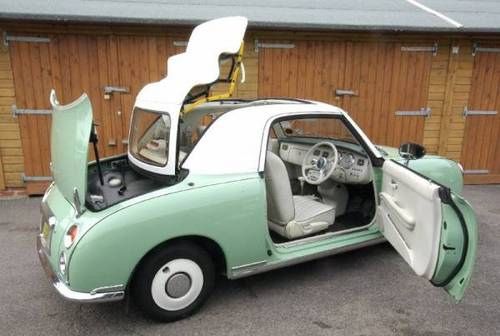 an old car with its doors open in a parking lot next to a wooden building