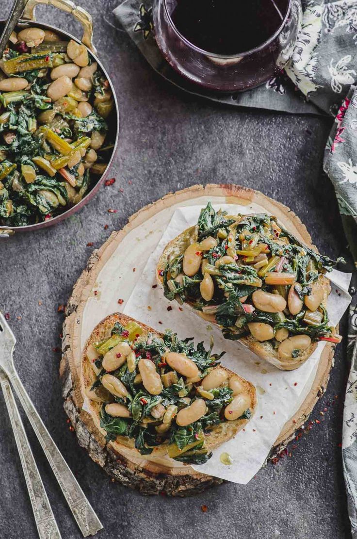 two pieces of bread with spinach and chickpeas on top next to silverware