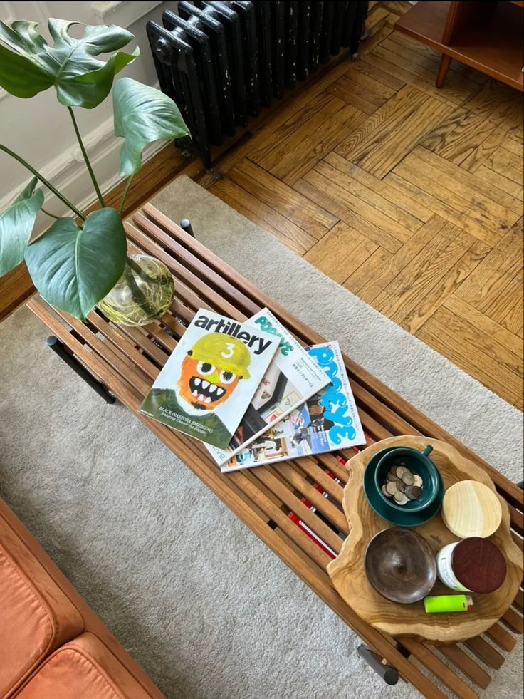 a coffee table with magazines and other items on it next to a plant in a living room