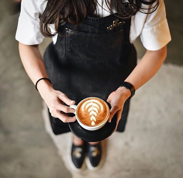 a woman holding a cup of coffee in one hand and an apron on the other