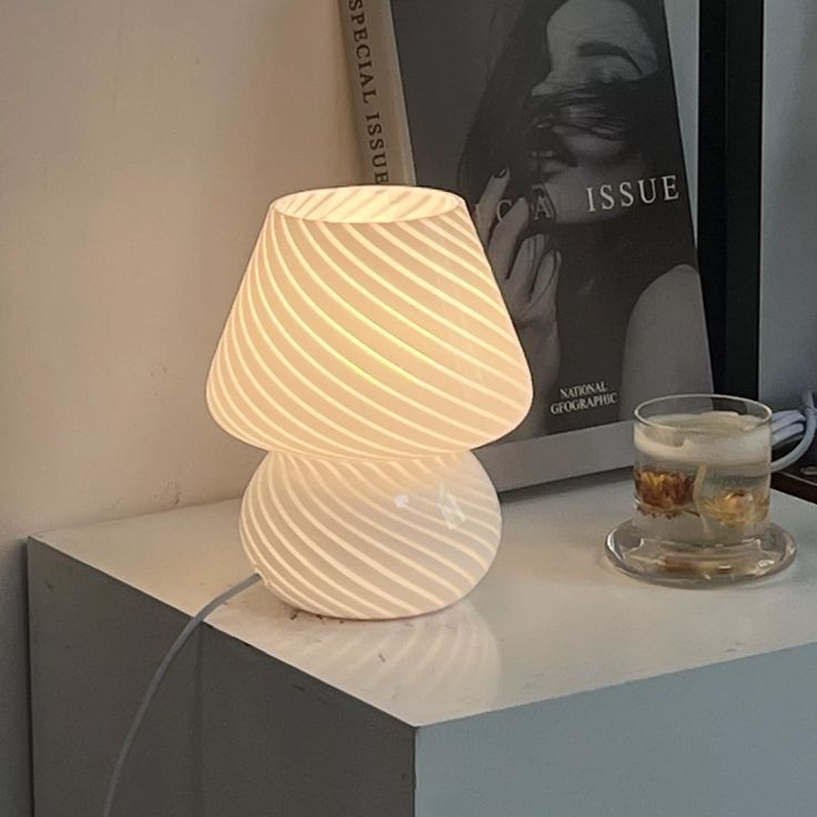 a white lamp sitting on top of a table next to a glass cup and book