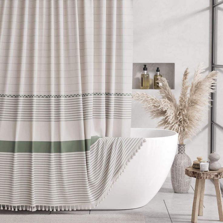 a bath tub sitting next to a shower curtain in a white bathroom with green and gray stripes