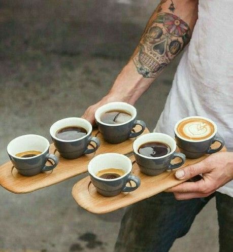 a man holding a wooden tray with cups of coffee on top of it and four other mugs in front of him