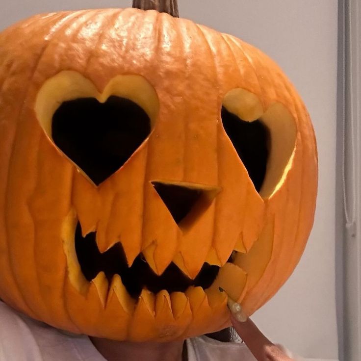 a person holding up a carved pumpkin with hearts on it's face and eyes