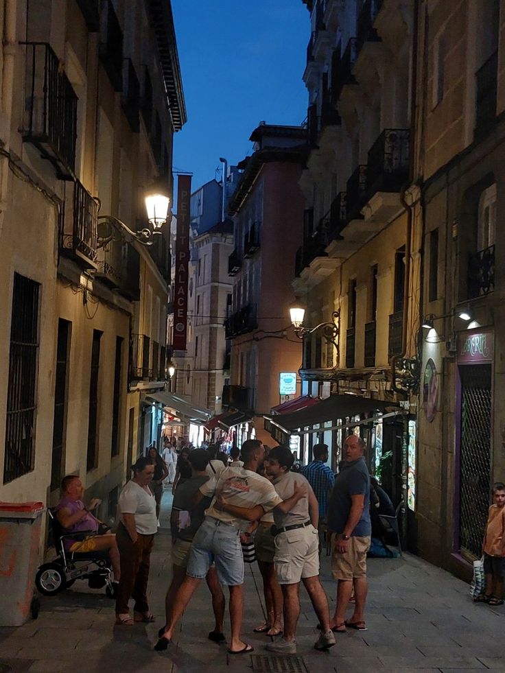 several people are huddled together on the sidewalk in an alleyway at night with buildings and street lights