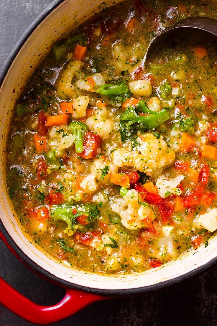 a pot filled with soup and vegetables on top of a wooden table next to a spoon