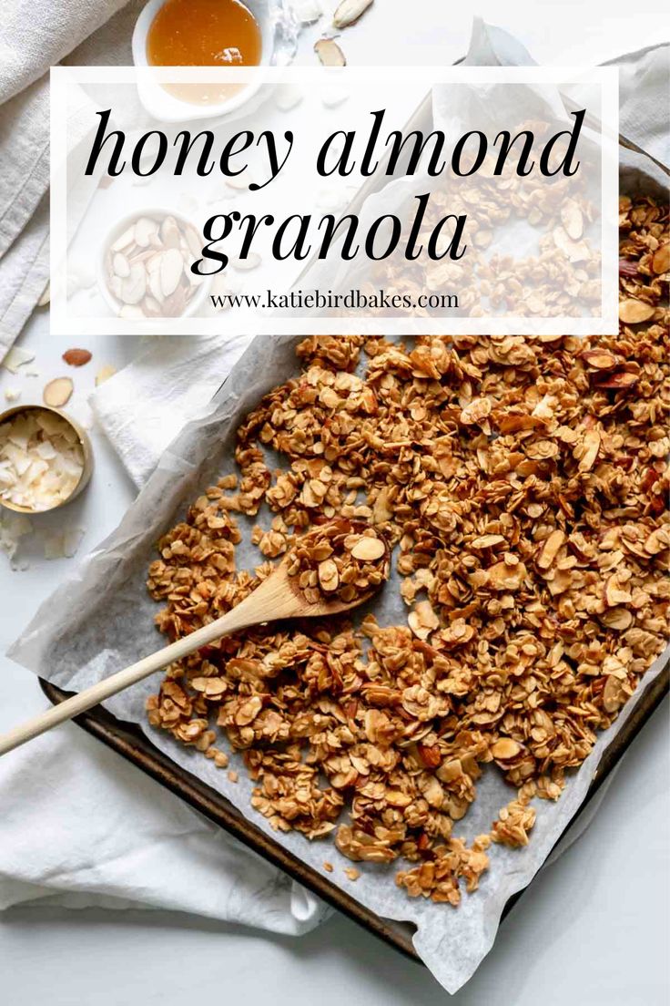 homemade granola on a baking sheet with a wooden spoon and bowl of honey in the background