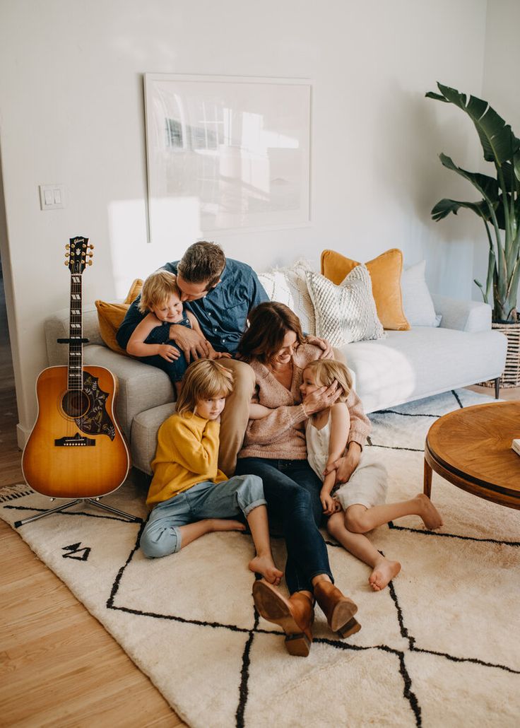 a group of people sitting on top of a couch in a living room next to a guitar