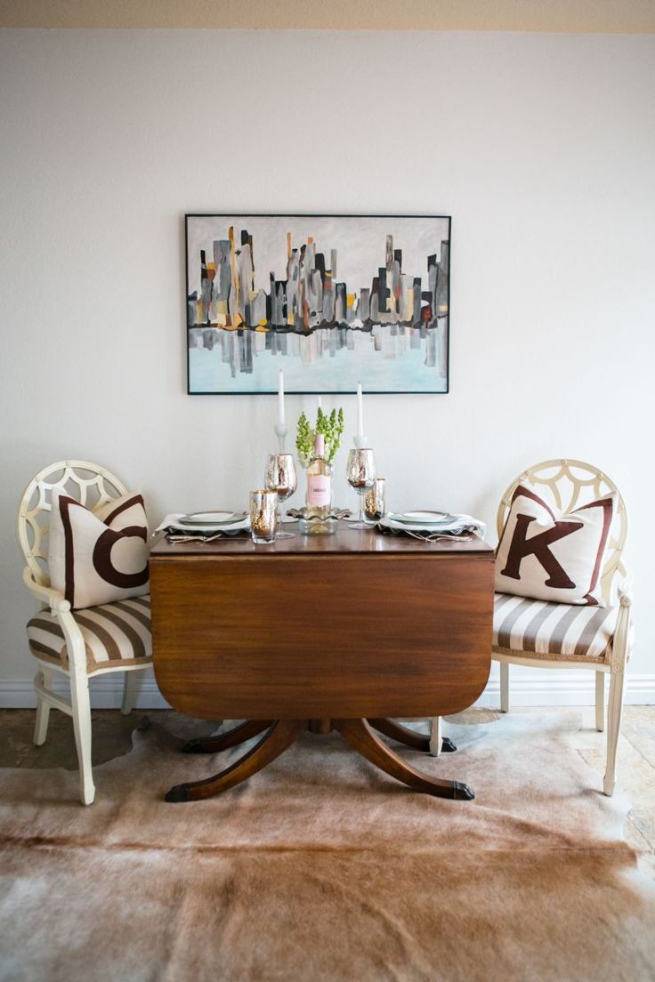 a dining room table with two chairs and a painting on the wall in the background