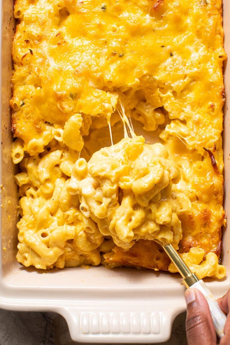 a casserole dish with macaroni and cheese being scooped from the casserole