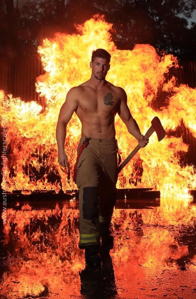 a shirtless firefighter standing in front of a large pile of flames holding an ax