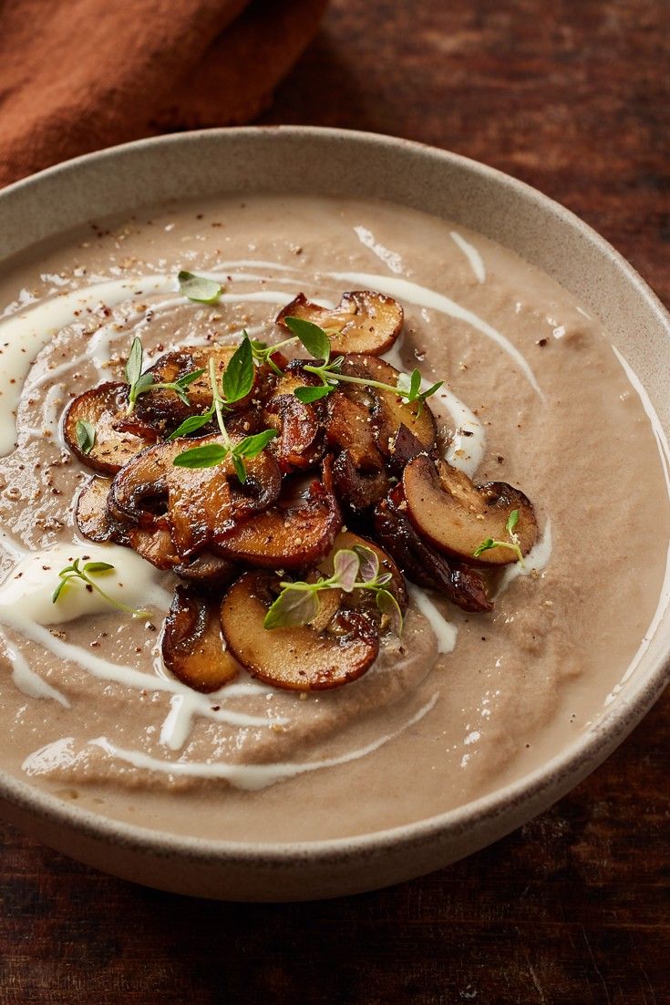 a white bowl filled with soup and mushrooms on top of a wooden table next to a napkin