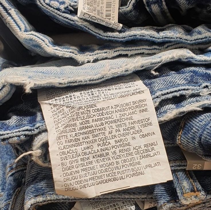 a pile of blue jeans sitting on top of each other with some paper pinned to them