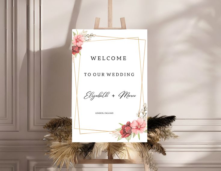 a welcome sign is displayed on an easel in front of a wall with flowers and feathers