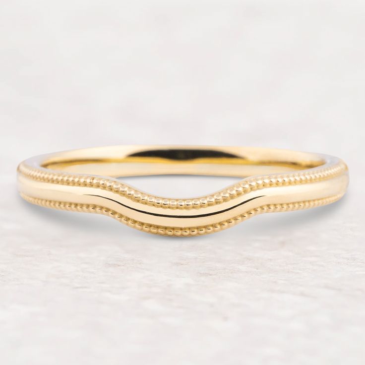 a yellow gold wedding band with beaded edges on a white marble surface, close up