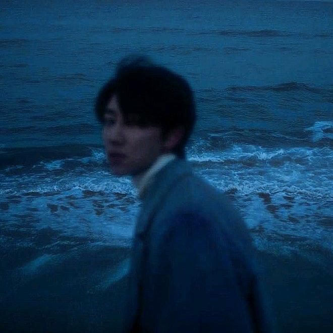 a man standing on top of a sandy beach next to the ocean at night time