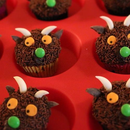 cupcakes decorated with brown frosting and green candies are arranged in the shape of a demon's head