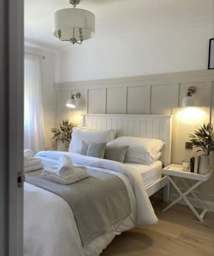 a bed with white linens and pillows in a bedroom next to a window that has potted plants on it