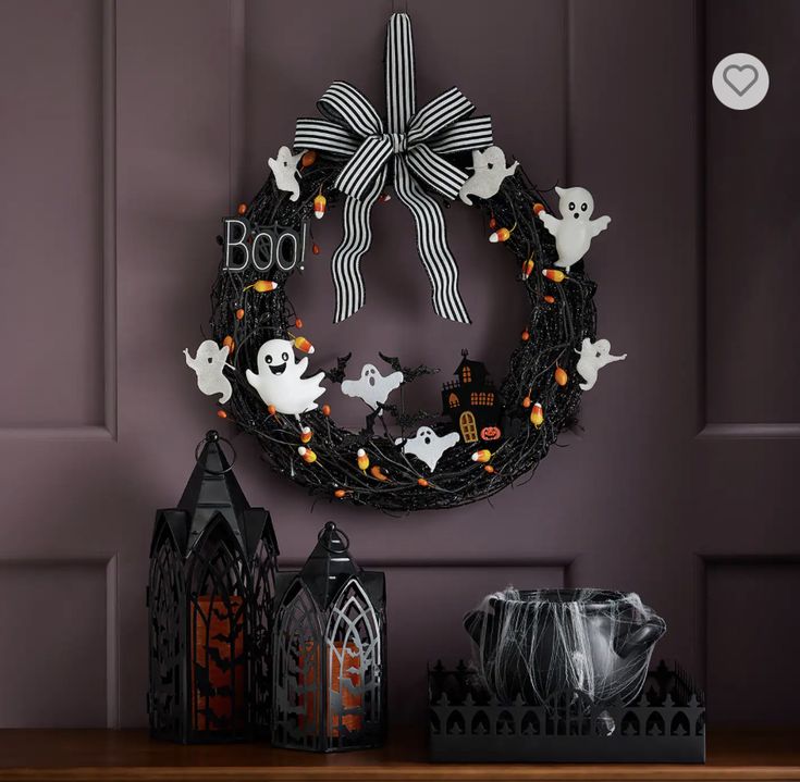 a halloween wreath with ghostes and pumpkins hanging on the wall next to candles