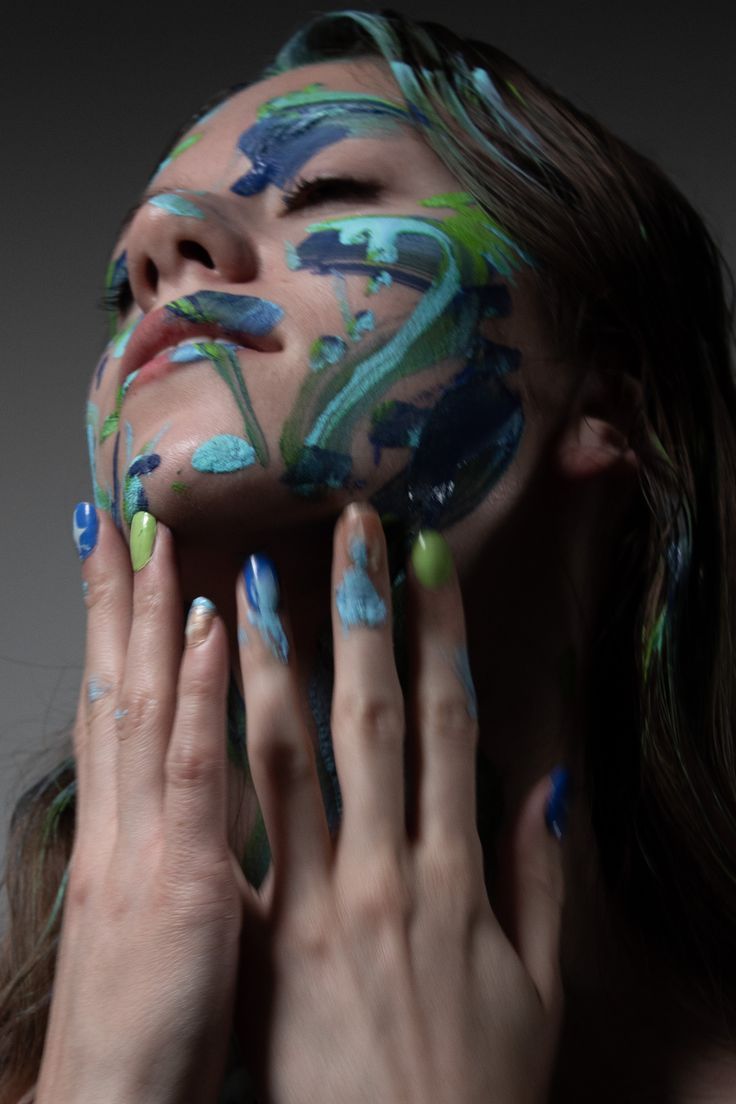 a woman with her face painted in blue and green, holding her hands up to her face