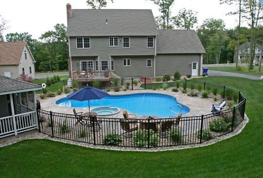 an above ground pool surrounded by a metal fence and patio area with chairs, table and umbrella