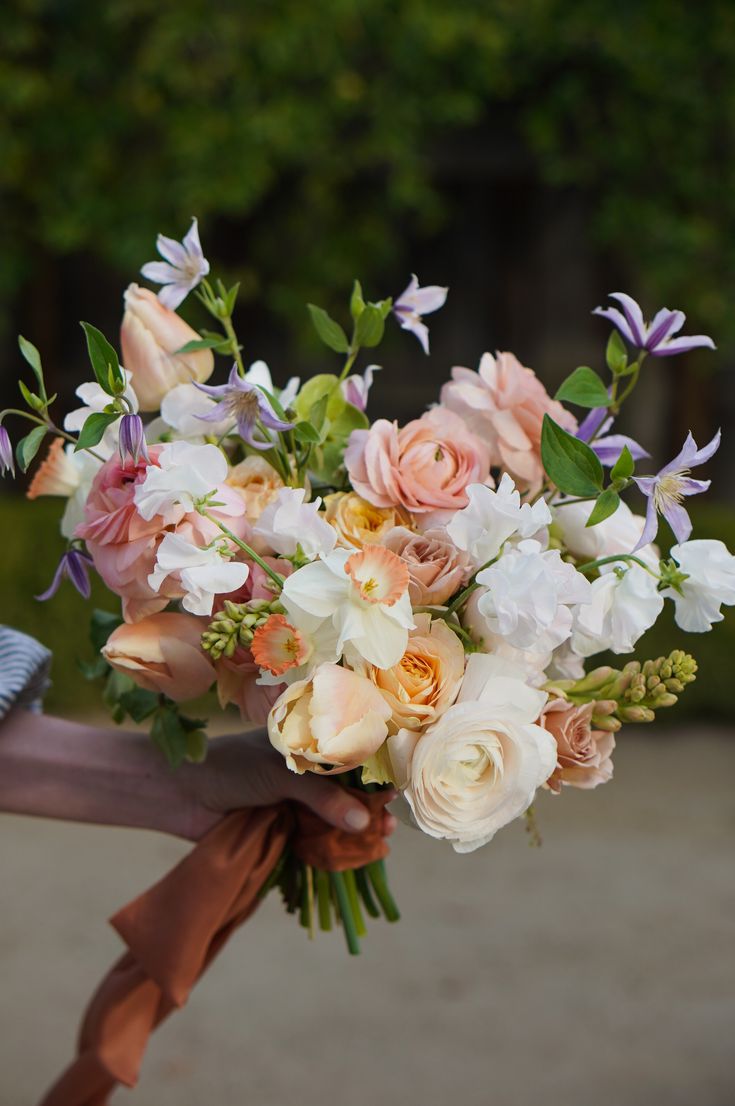 a bouquet of flowers is held by someone's hand in front of some trees