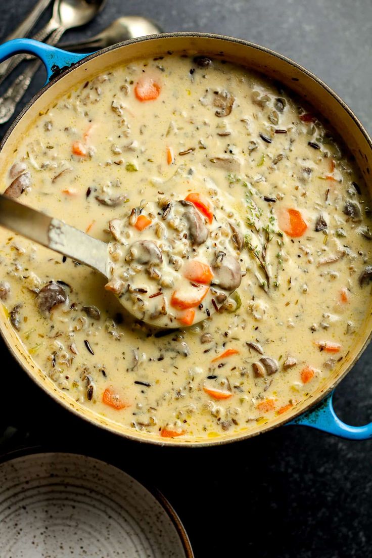 a blue pot filled with soup on top of a stove next to two plates and spoons