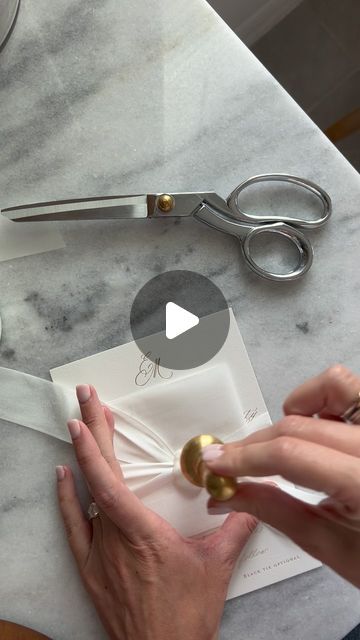 a person cutting paper with scissors on top of a marble table next to other items