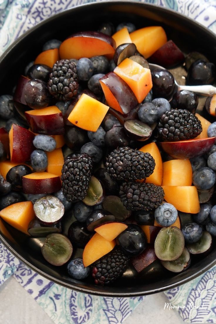 berries, peaches, and other fruits are in a bowl on a tablecloth