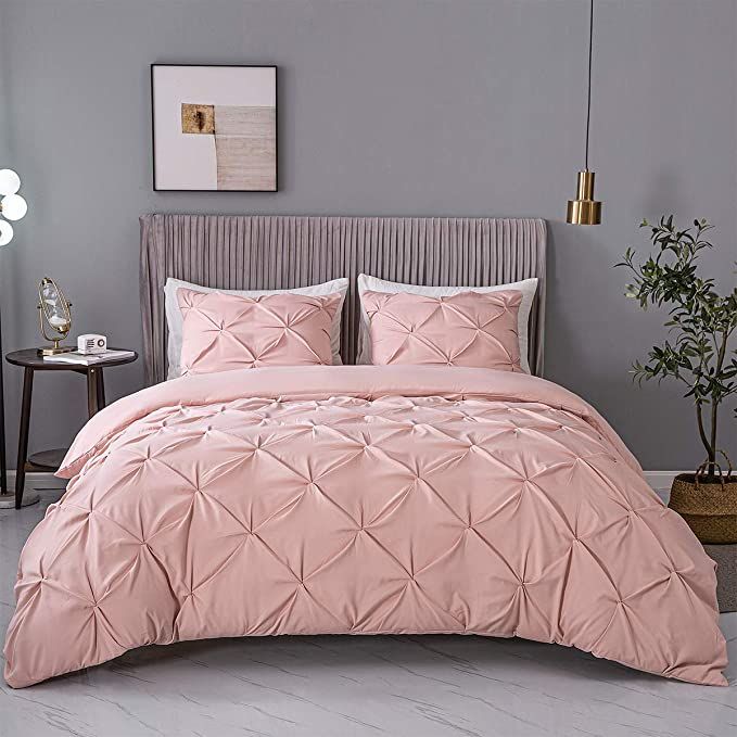 a bed with pink comforter and pillows in a room next to a plant on the floor