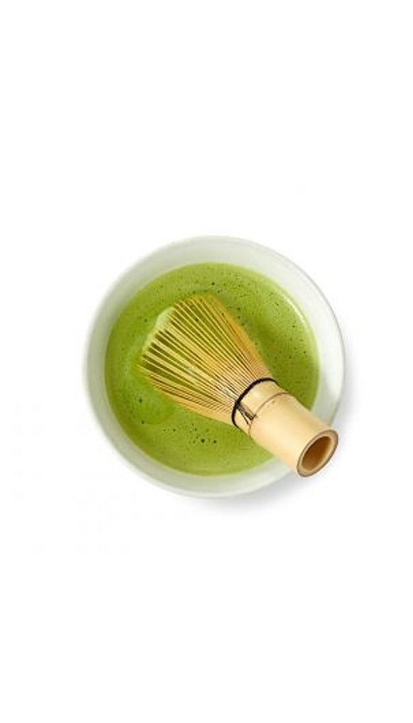 a whisk in a white bowl with green liquid and a bamboo stick sticking out of it