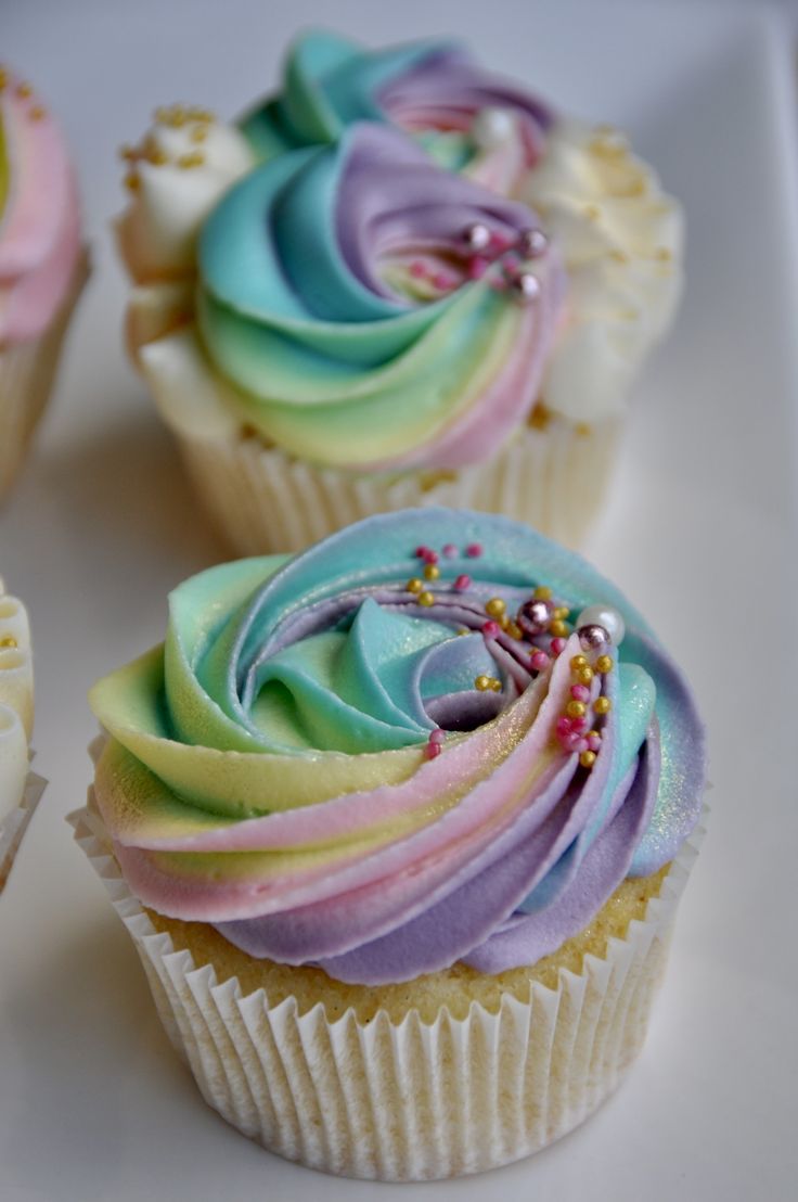 three cupcakes with different colored frosting on them sitting on a white plate