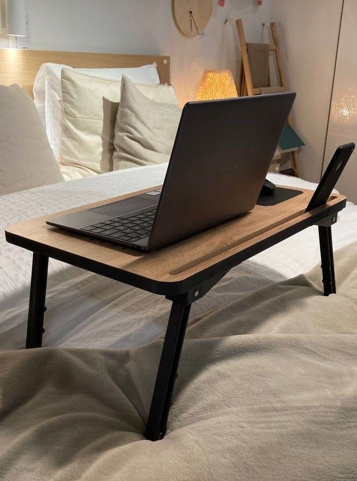 a laptop computer sitting on top of a wooden table in front of a white bed