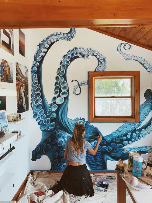 a woman sitting on top of a bed in front of a wall with an octopus painted on it