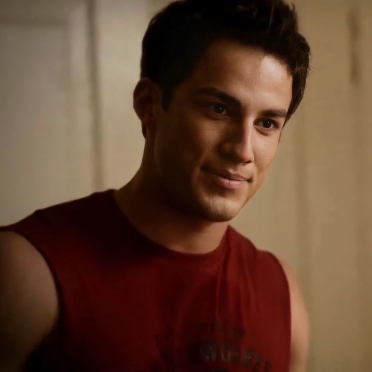 a young man in a red shirt is smiling at the camera and looking into the camera