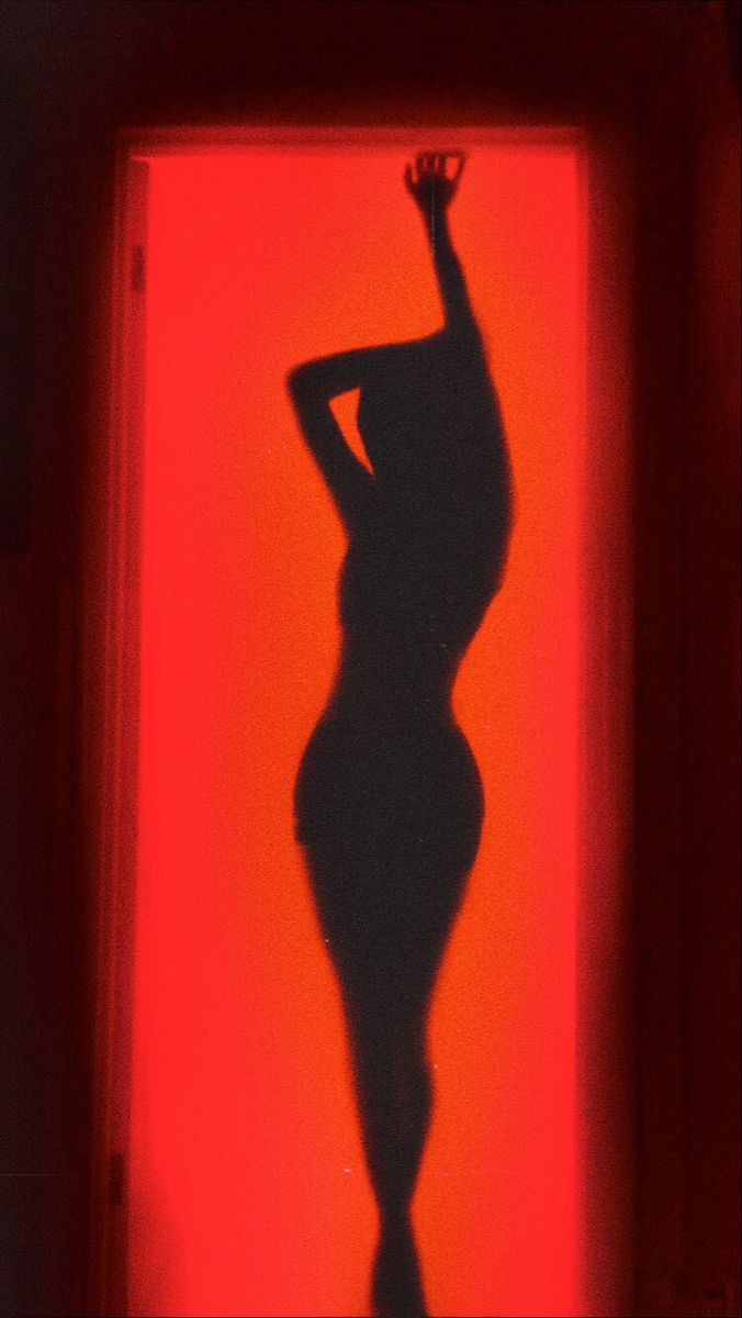 the silhouette of a woman standing in front of a red wall