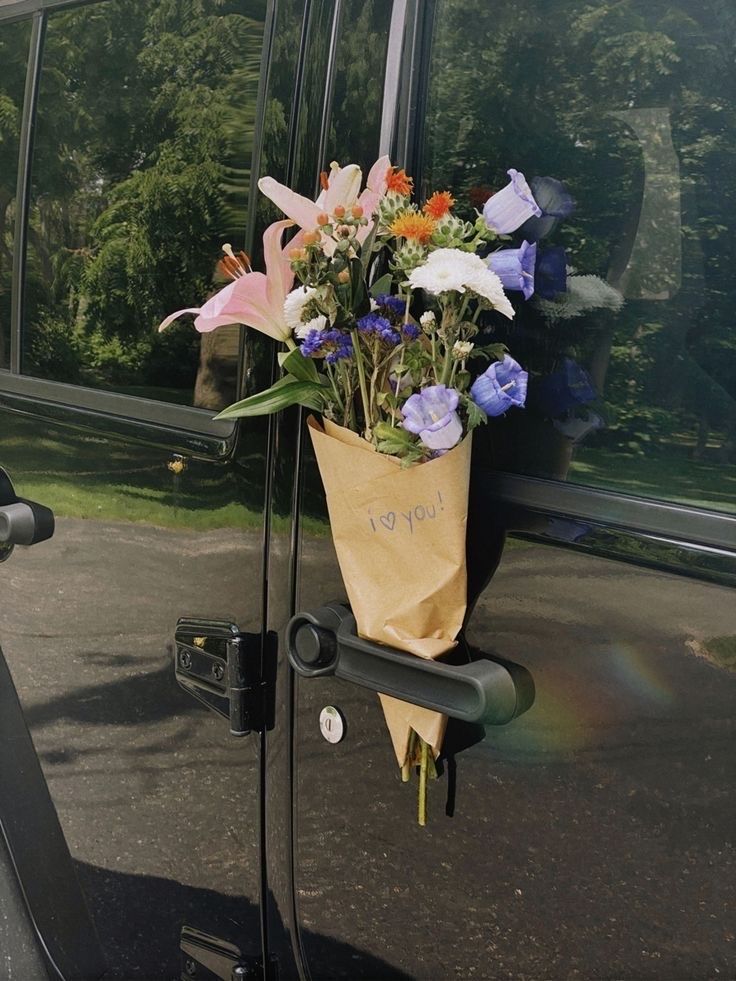 a bouquet of flowers in a brown paper bag hanging from the side of a vehicle