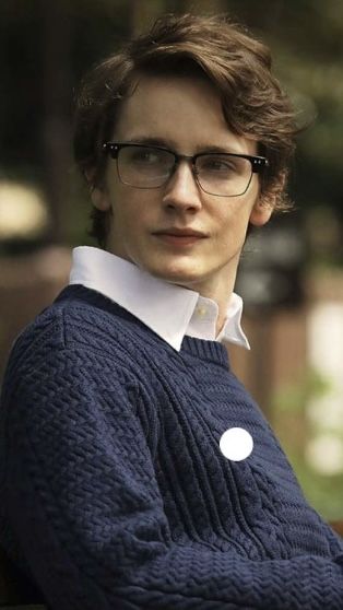 a woman with glasses is sitting on a bench and looking off to the side while wearing a blue sweater