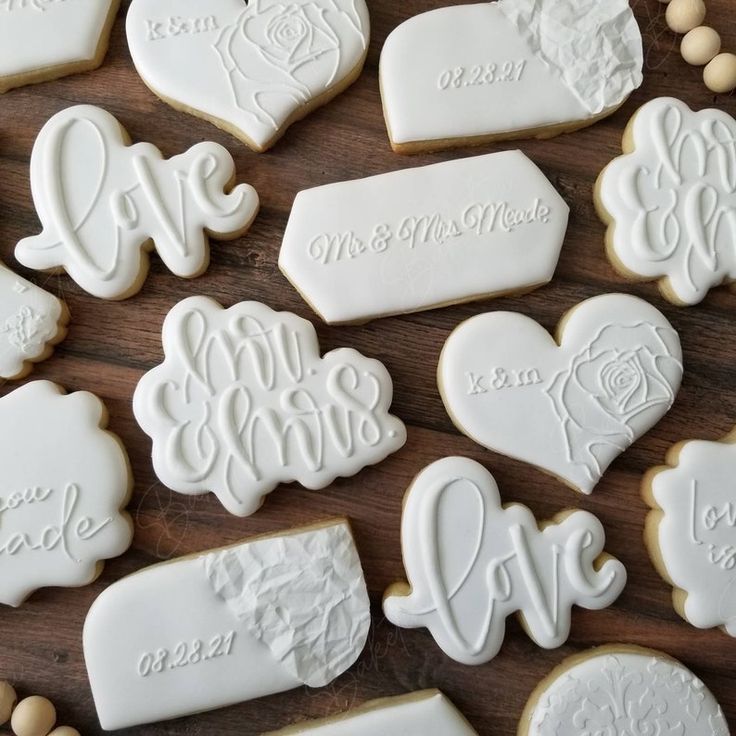 wedding cookies decorated with white icing on top of a wooden table next to chocolate candies