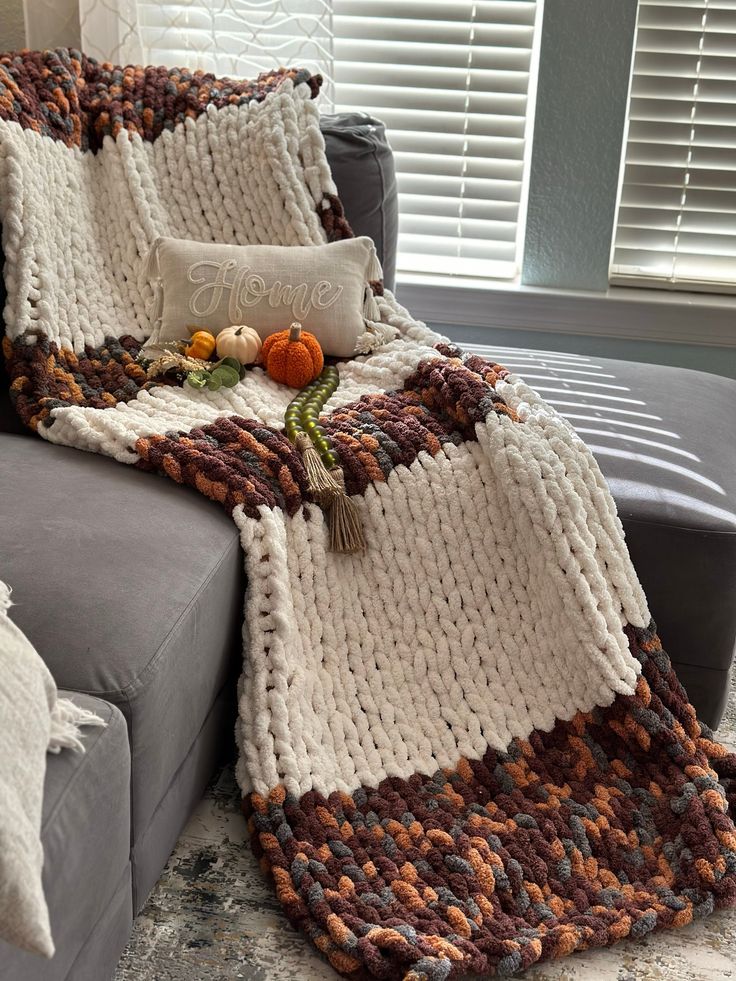 a couch with a knitted blanket on top of it next to pillows and pumpkins