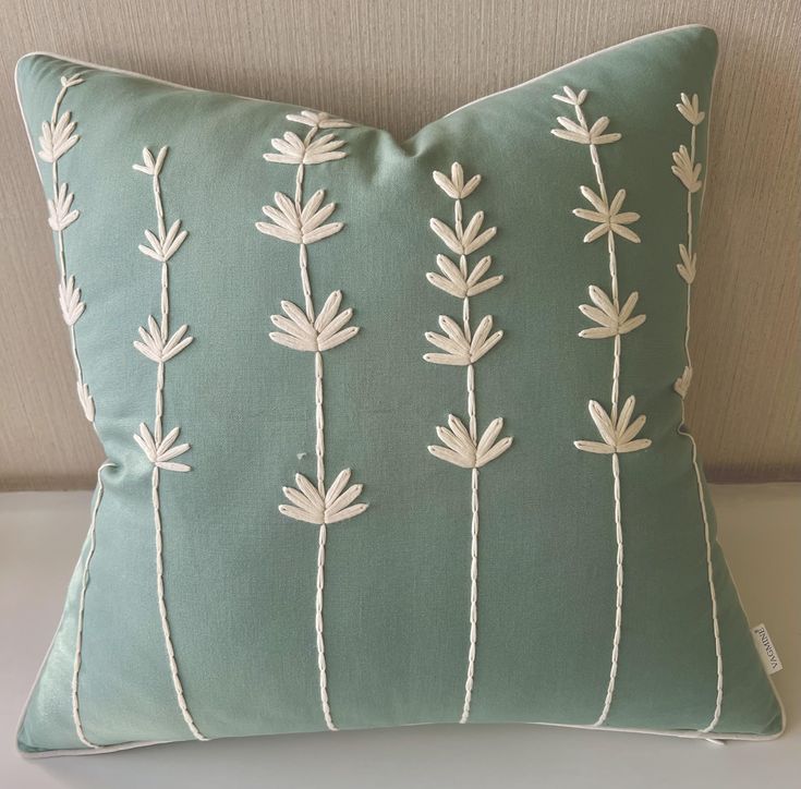 a green pillow with white flowers on the front and back, sitting on a couch