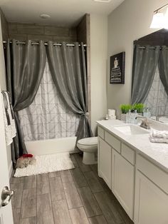 a bathroom with a toilet, sink and bathtub next to a window covered in gray curtains