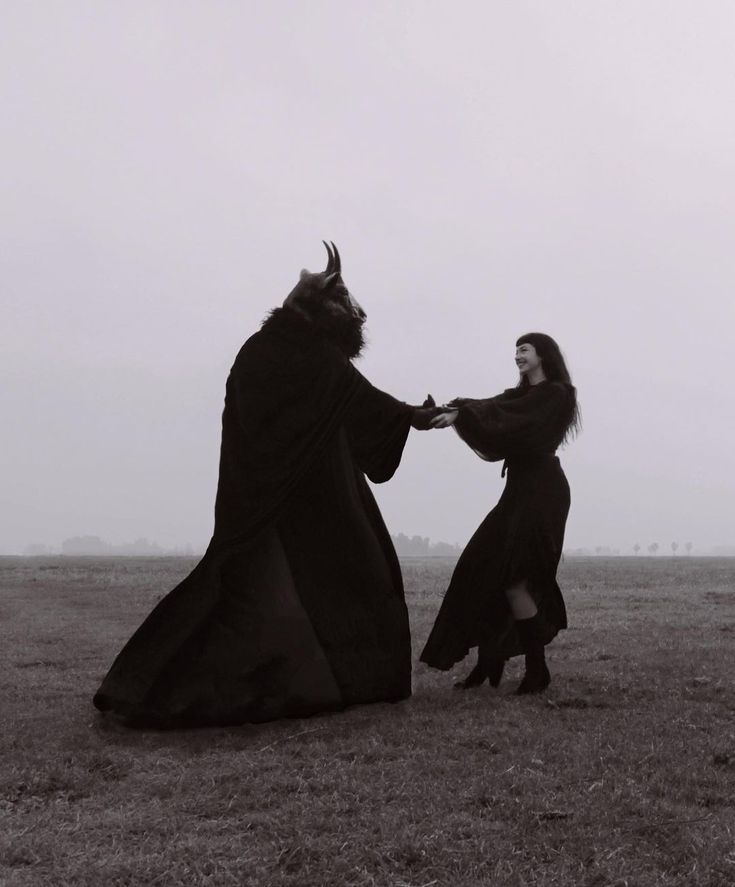 two people dressed in black holding hands and facing each other on a field with fog